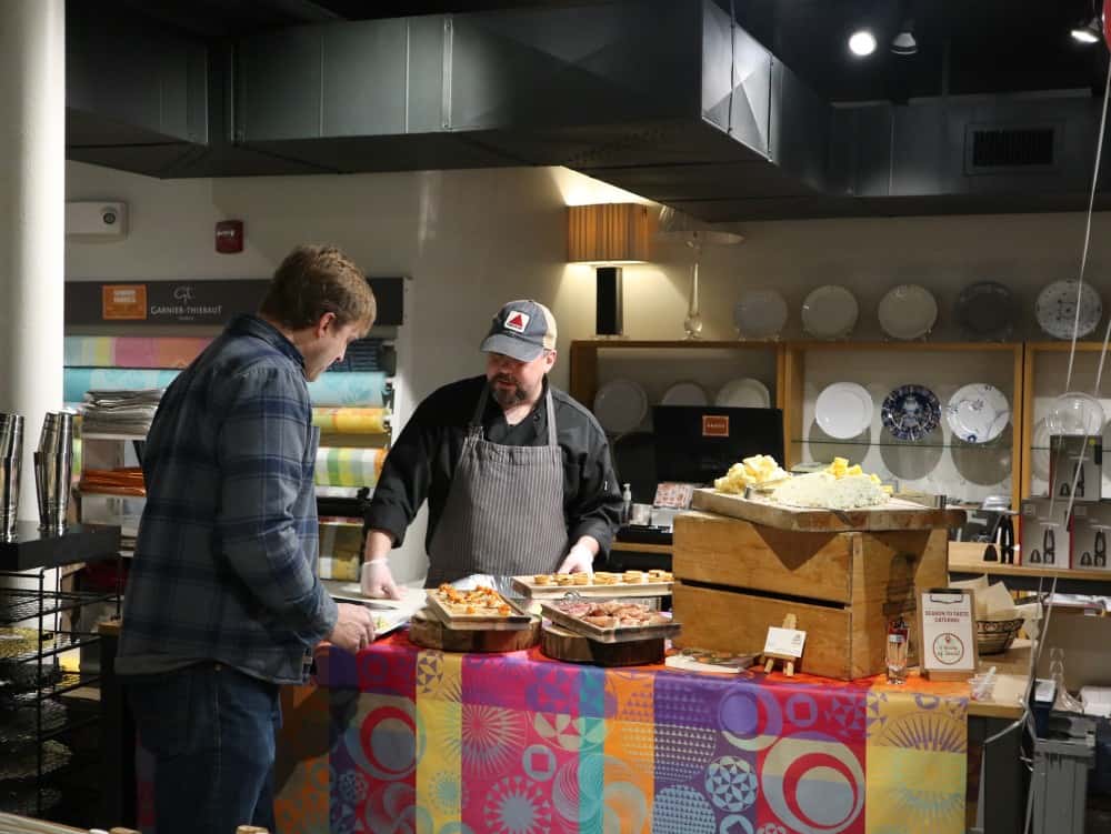 Two men stand at a table with various food dishes displayed